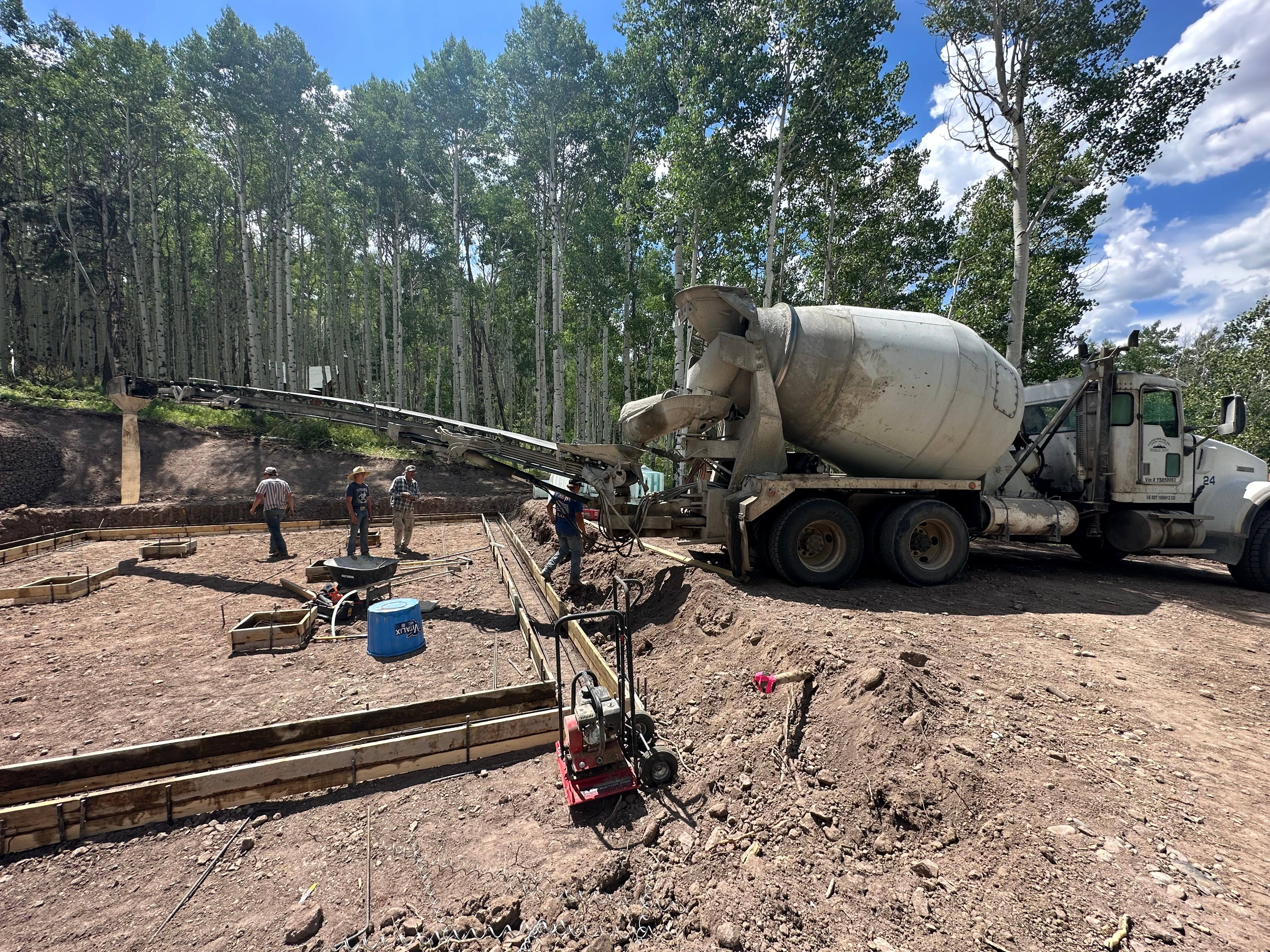 Concrete mixer truck pouring a residential foundation surrounded by aspen trees in Colorado