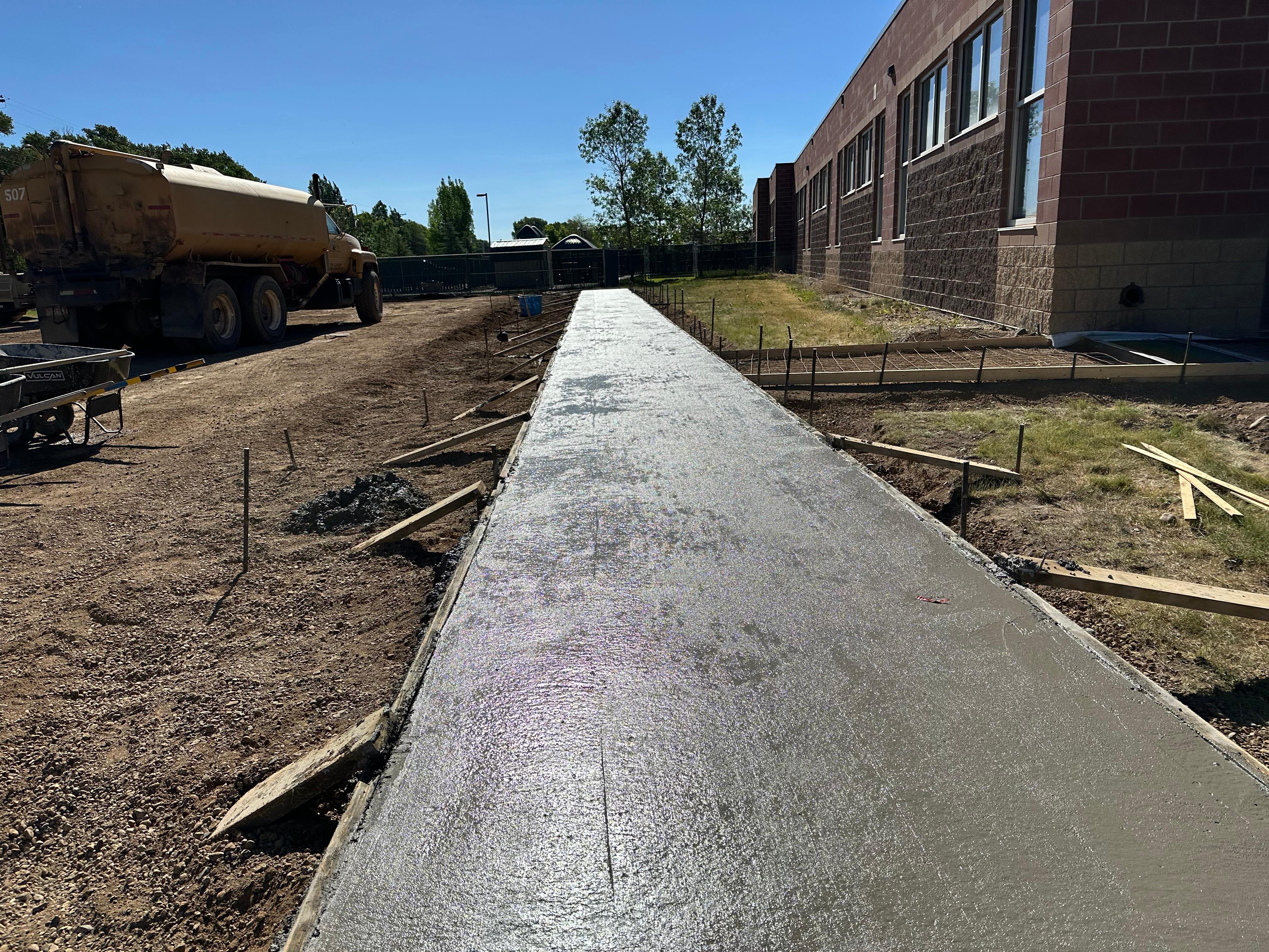 Freshly poured concrete sidewalk alongside a building with mixer truck on site